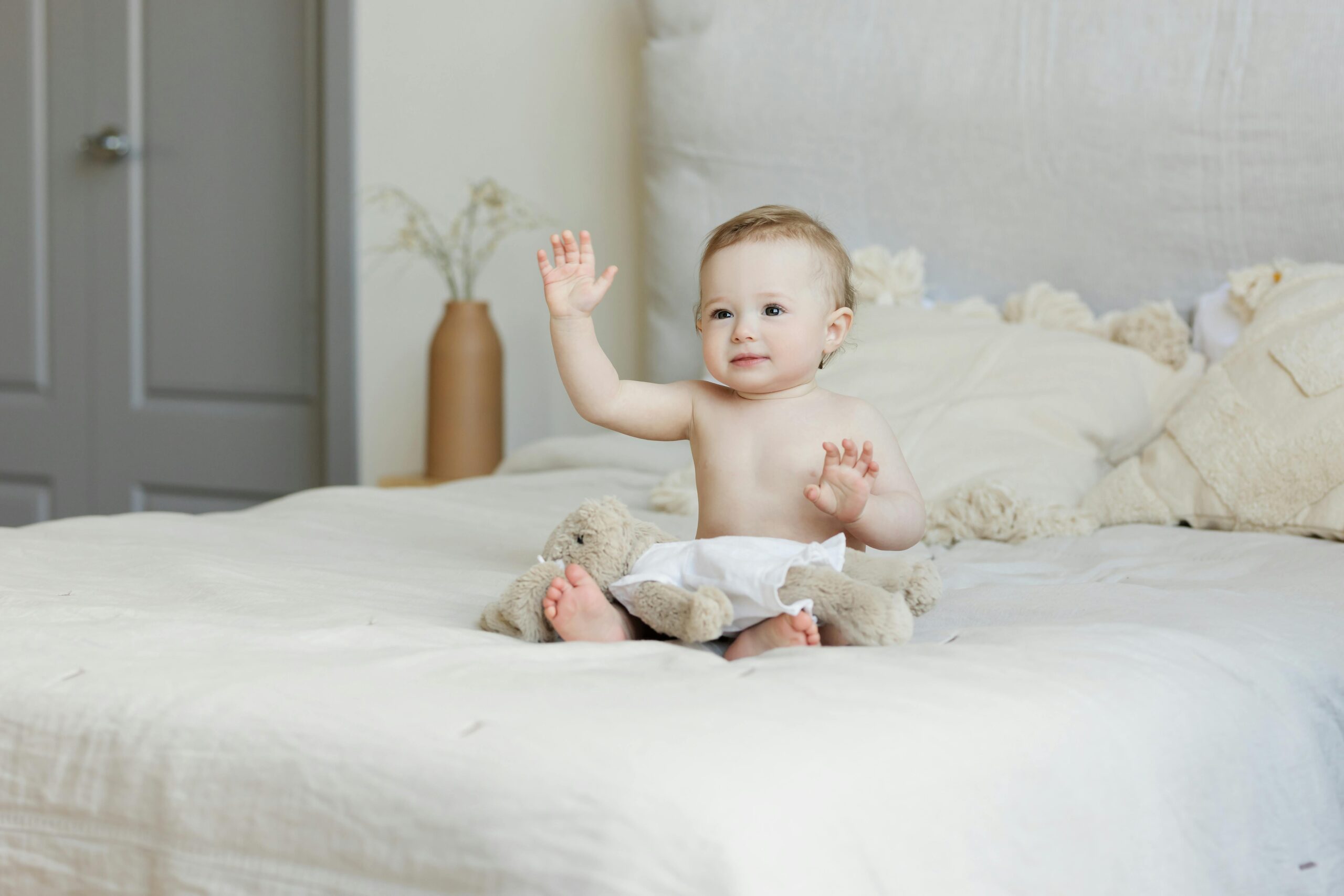 A cute baby happily sitting on a bed with plush toys, radiating a joyful expression.