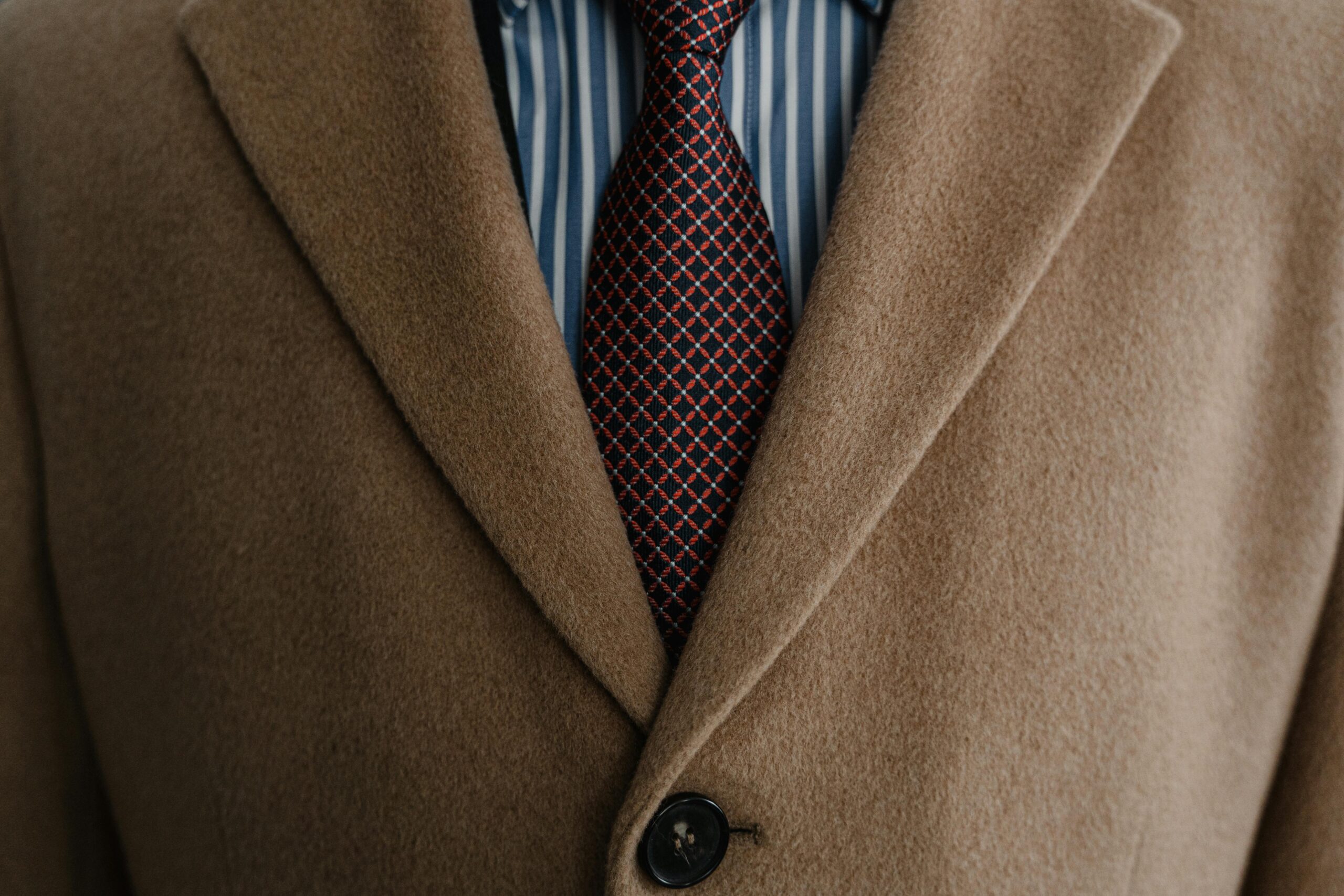 Close-up of a sophisticated brown wool coat over a striped shirt and patterned tie.